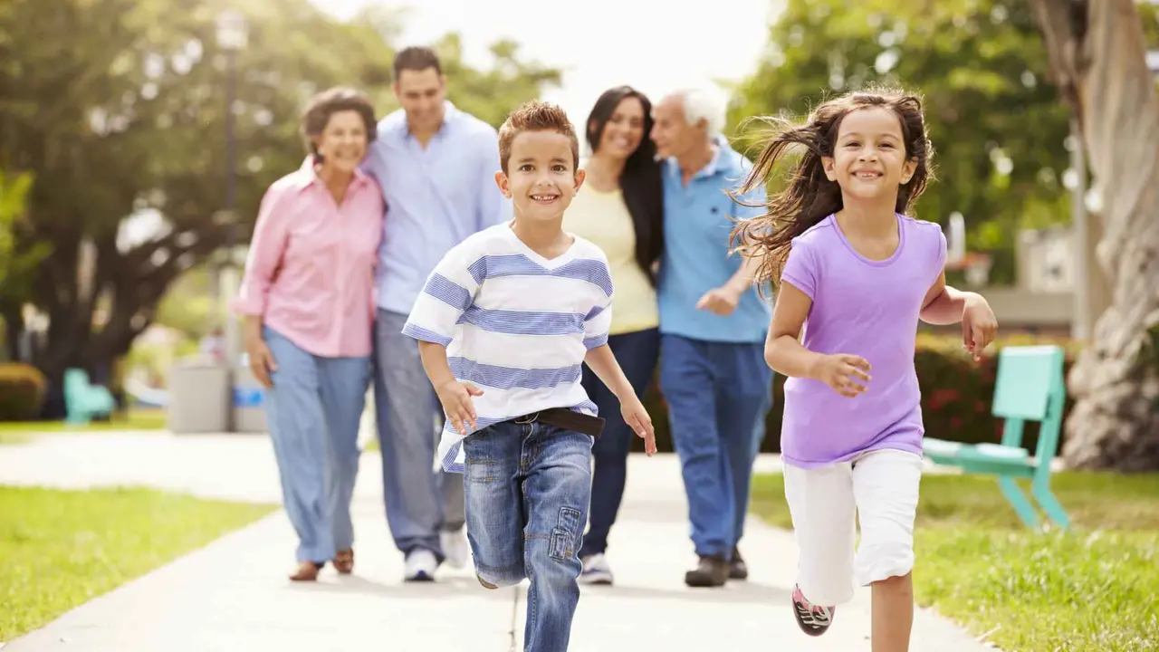 Multi Generation Family Walking In Park Together Children Running Ahead.