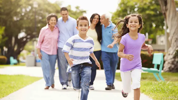 Multi Generation Family Walking In Park Together Children Running Ahead.