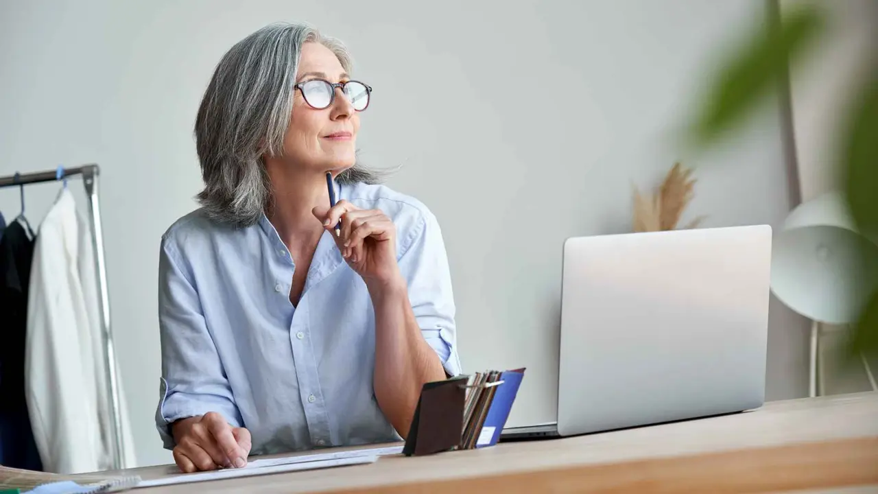 A woman smiles as she sits in front of her laptop and plans her retirement.