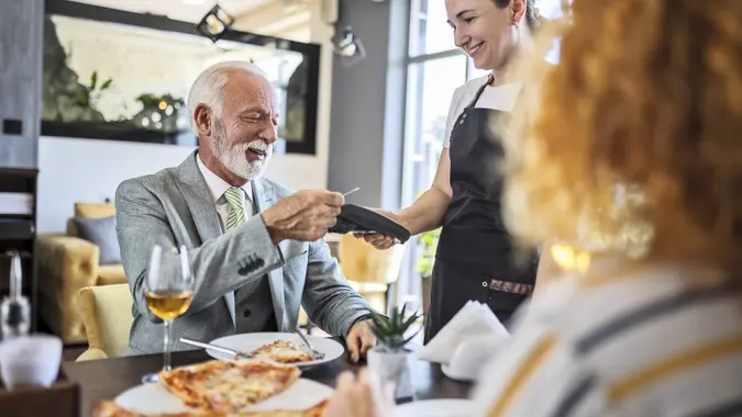 Father eating pizza with daughter in restaurant and paying the bill stock photo