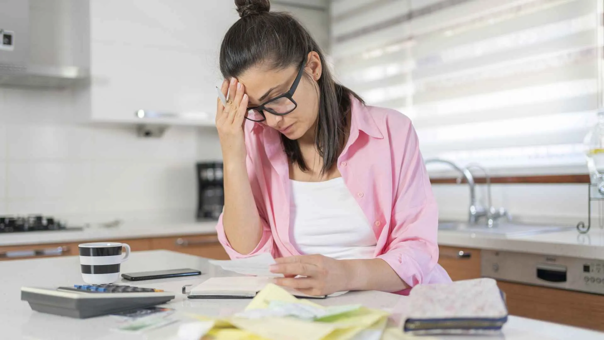 A woman looks sad and frustrated as she goes through her bills.