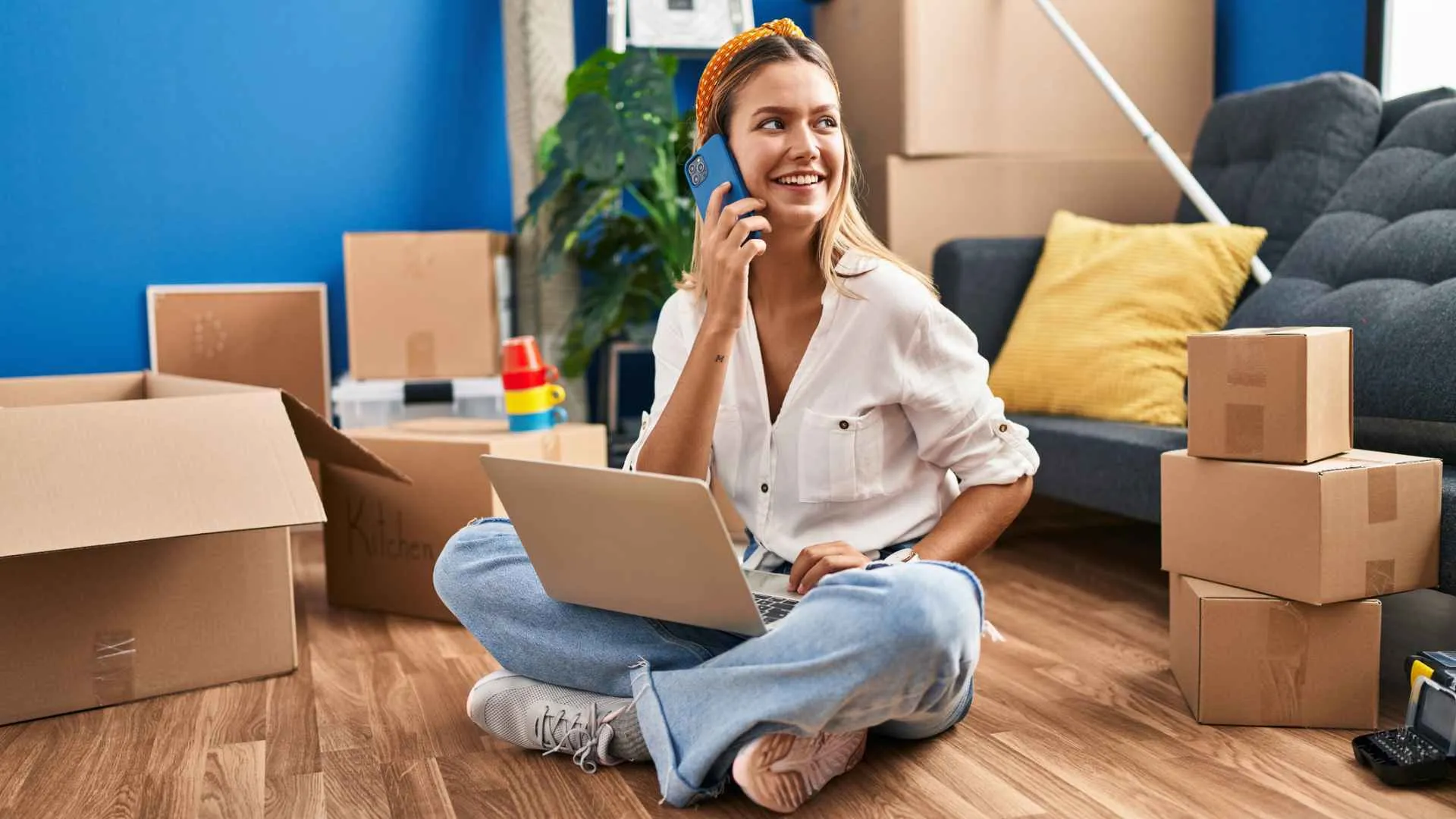 Young woman using laptop and talking on smartphone at new home.