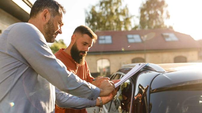 Copy space shot of mid adult man selling his old car and giving customer a clipboard to sign after he purchased it.