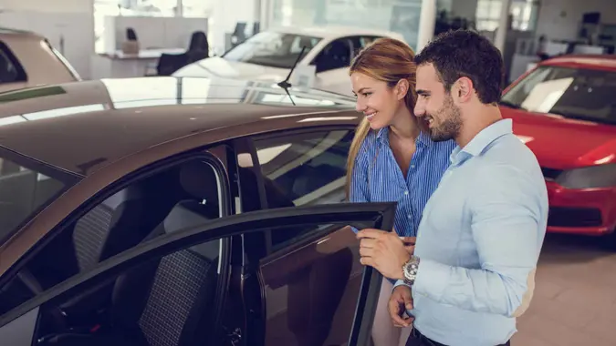Smiling couple looking for a new car to buy at car showroom.