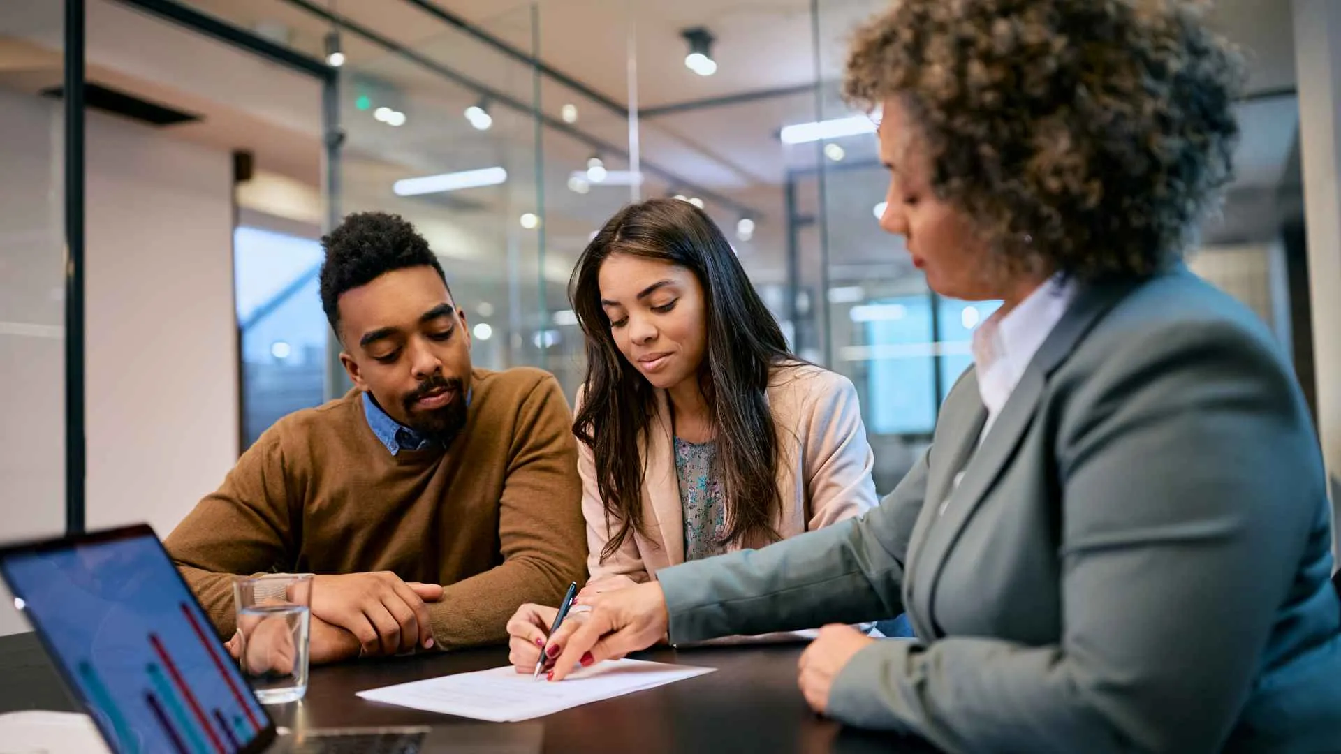 African American woman and her husband signing mortgage agreement during a meeting with their bank manager.