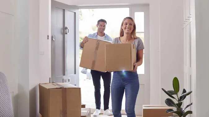 Excited Couple Carrying Boxes Through Front Door Of New Home On Moving Day.
