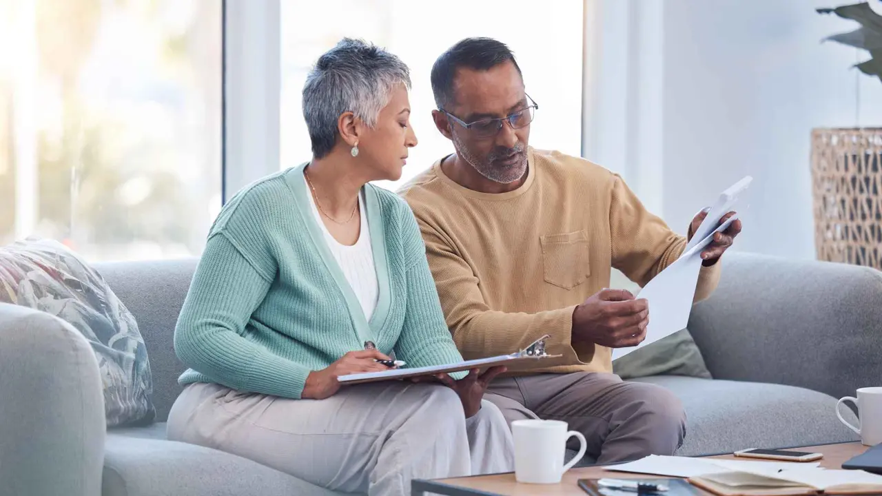 A couple sitting on a couch reviewing financial statements together, planning their budget and managing expenses.