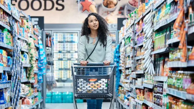 Black woman, customer and grocery shopping cart in supermarket store, retail outlet or mall shop.