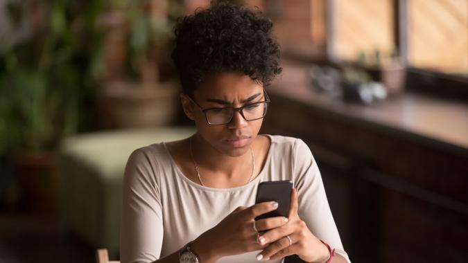 Upset confused african woman holding cellphone having problem with mobile phone, frustrated angry mixed race girl reading bad news in message looking at smartphone annoyed by spam or missed call.