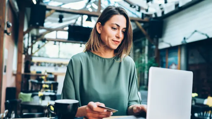 A young woman shops on her laptop while holding a credit card.