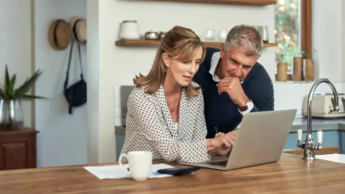 A senior couple planning their finance and paying bills while using a laptop at home.