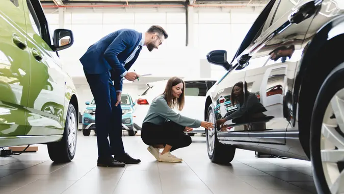 customer choosing new car, trying checking its options, tire, wheels while male shop assistant helping her to choose it at dealer auto shop stock photo