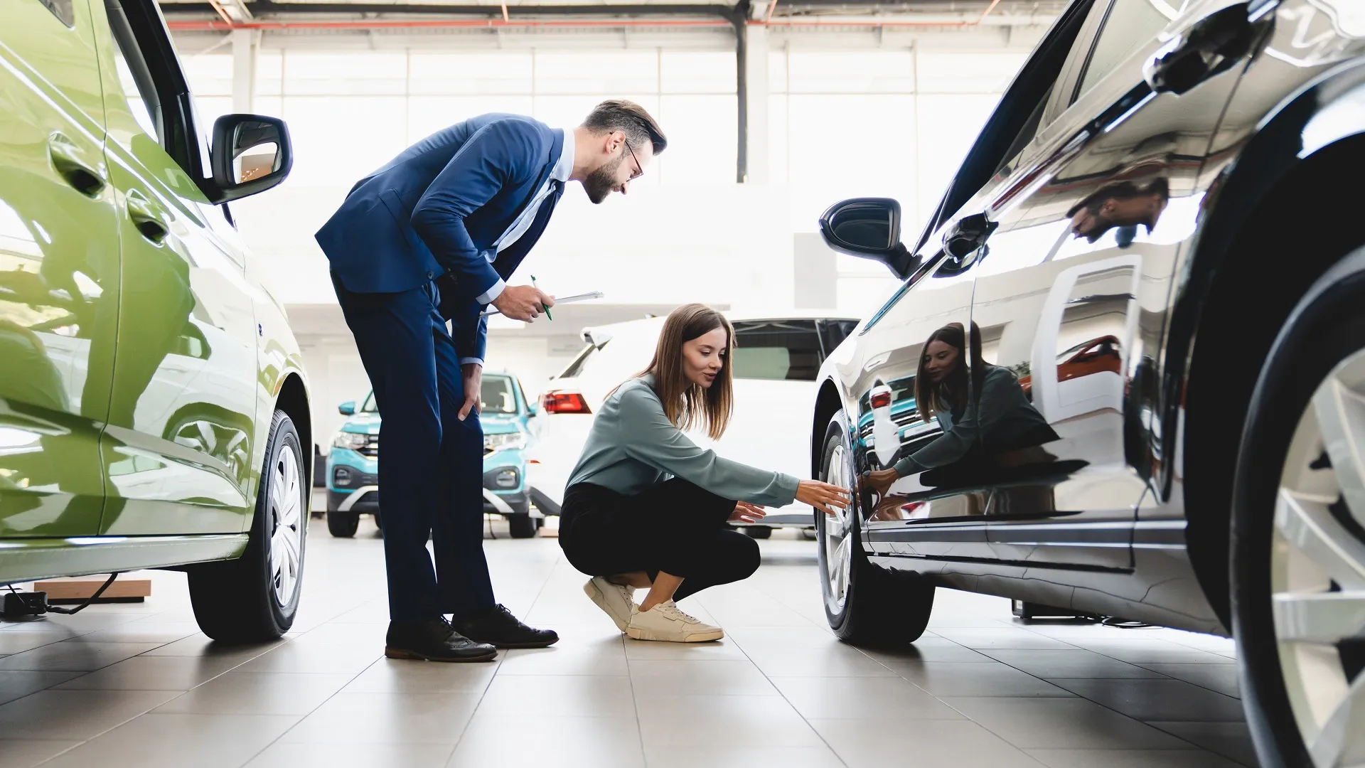 Beautiful young caucasian female client customer choosing new car, trying checking its options, tire, wheels while male shop assistant helping her to choose it at dealer auto shop stock photo