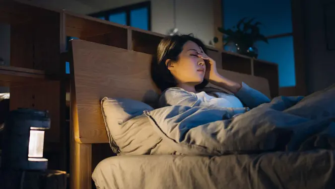 Young Asian woman feeling sick and suffering from a headache, lying on bed and taking a rest at home.