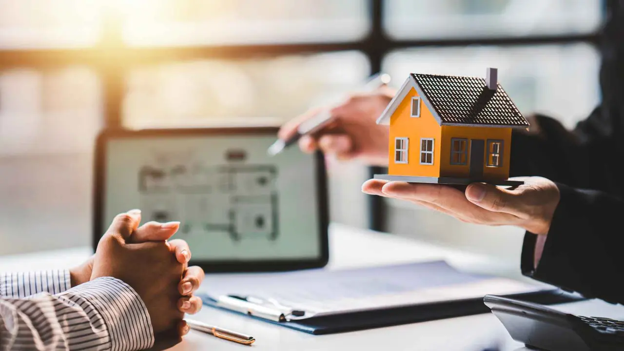 Mortgage broker explaining loan paperwork to a client, with documents and a laptop during a real estate financing meeting.