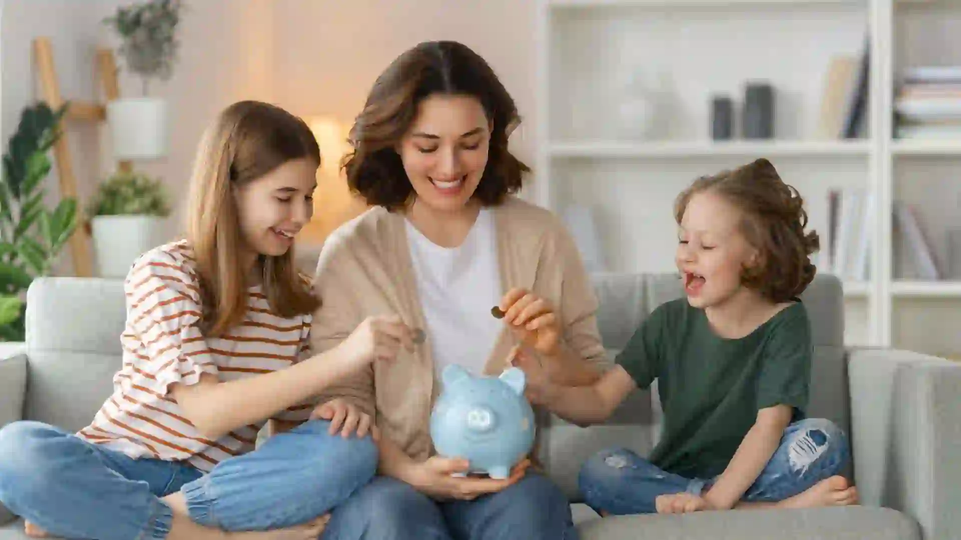 A woman holds a piggy bank and sits with her children on a couch as they learn about saving money.