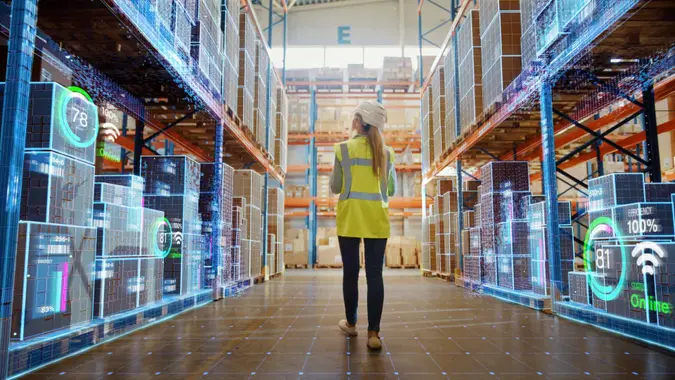 Futuristic Technology Retail Warehouse: Worker Doing Inventory Walks when Digitalization Process Analyzes Goods, Cardboard Boxes, Products with Delivery Infographics in Logistics, Distribution Center.
