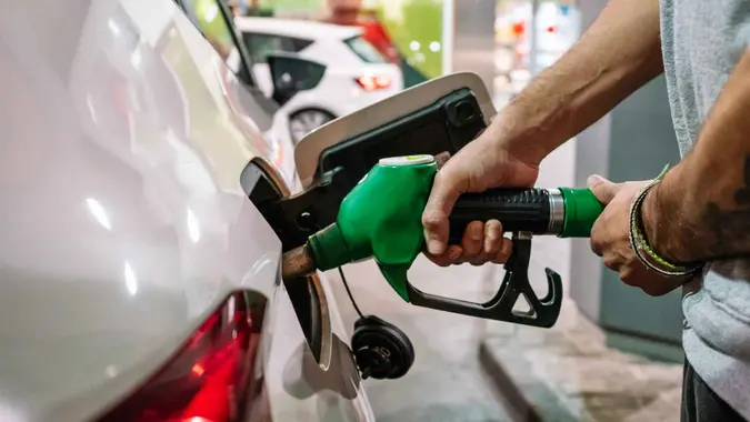 Unrecognizable male putting fuel dispenser in tank while refueling vehicle on self service gas station.