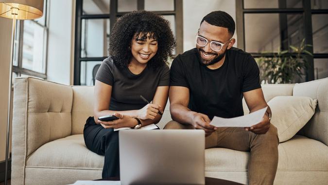 A couple smiles as they over their finances and work on their laptop.