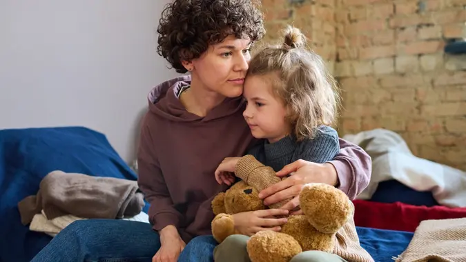 Young woman giving hug to her cute little son with brown soft teddybear stock photo