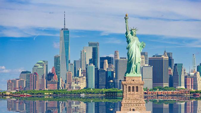 Statue of Liberty and New York City Skyline with Manhattan Financial District, Battery Park, Water of New York Harbor, World Trade Center, Empire State Building, Governors island and Blue Sky with Puffy Clouds.