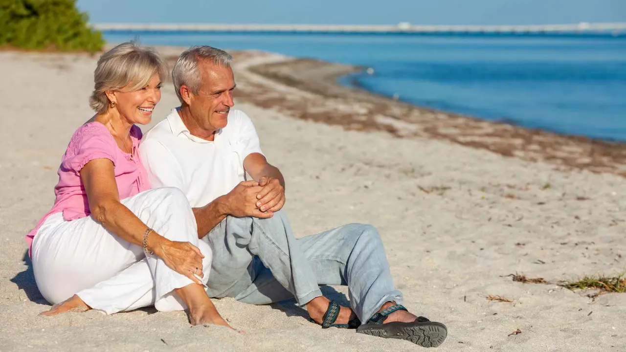 Happy senior man and woman couple sitting on a sunny beach, smiling and laughing.