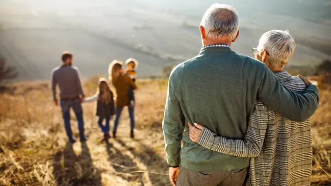 Rear view of embraced senior couple looking at their family in nature. stock photo