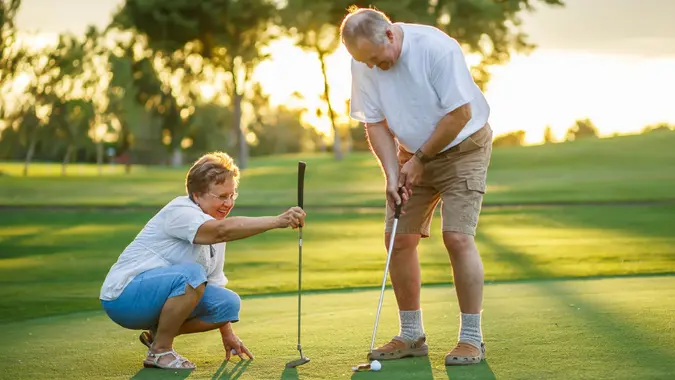 Active senior lifestyle, elderly couple playing golf together at sunset stock photo