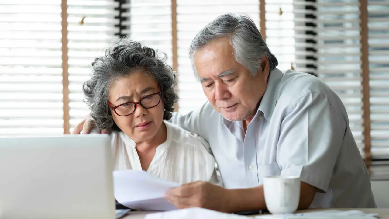 A stressed Asian senior couple calculates their monthly expenses on a laptop computer.
