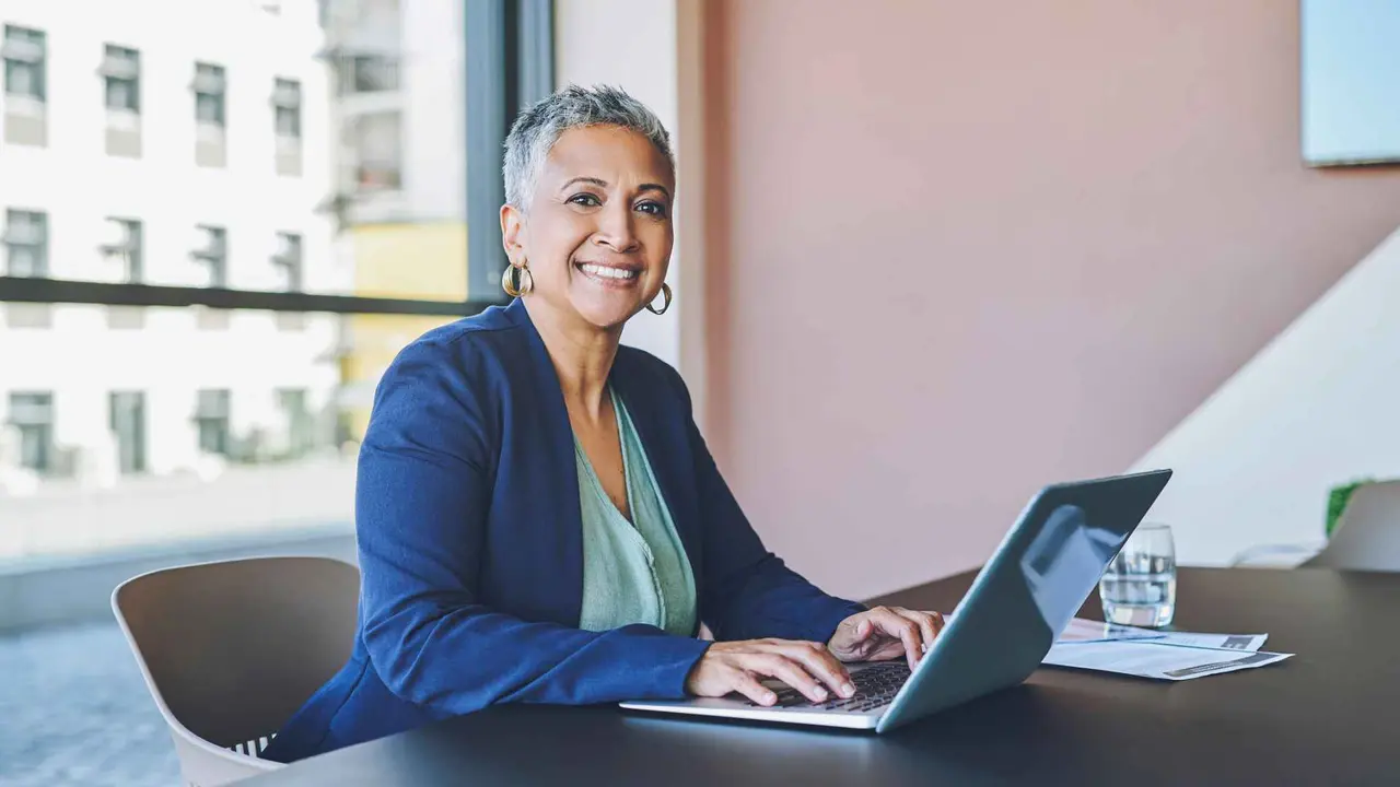 Femme d'affaires senior tapant sur un ordinateur portable, répondant aux e-mails et travaillant sur une proposition dans un bureau au travail.