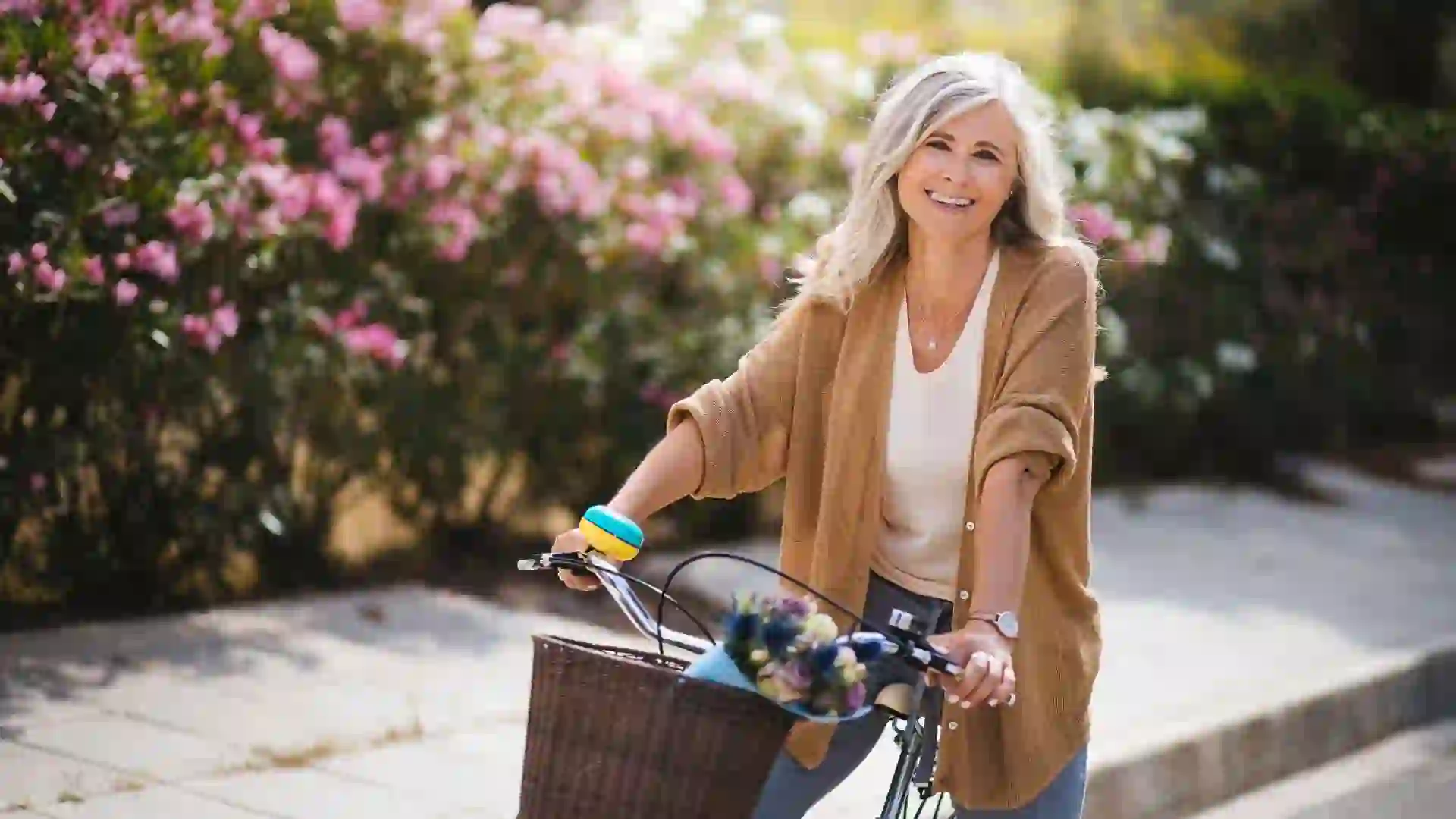 Happy active mature woman in fashionable clothes riding bicycle on suburban neighborhood street in spring.