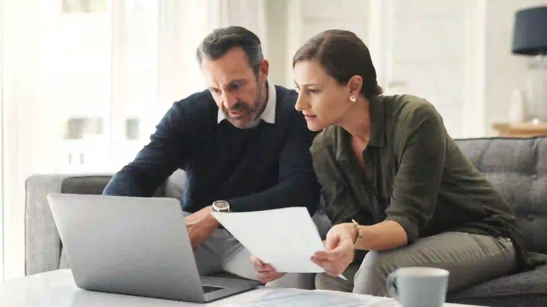 A couple reviews their financial documents on a laptop.