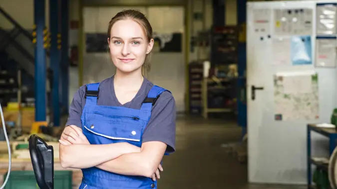 Portrait of a smiling young female trainee in metal industry, arms crossed.