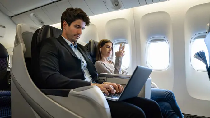 Portrait of a business man traveling by plane and working on his laptop computer - business trip concepts.