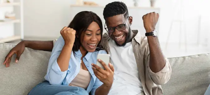 Couple sitting on a couch in the living room and reading great news.