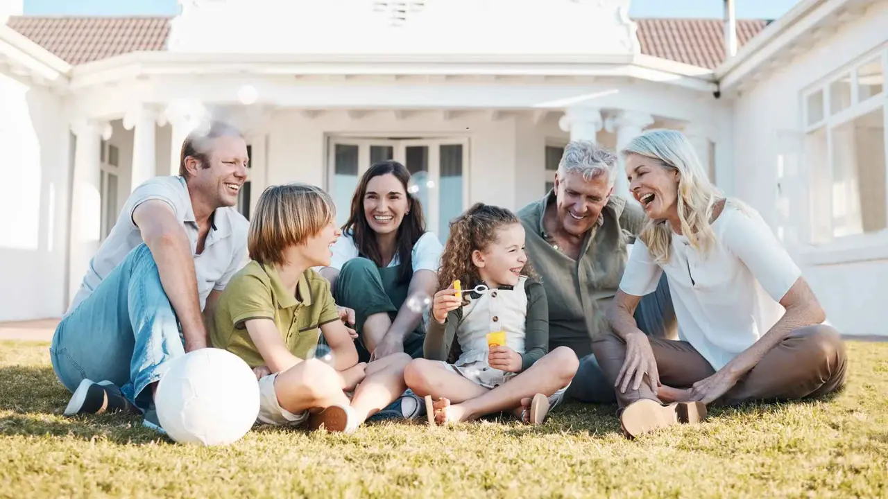 An intergenerational family spends time together outside their home while sitting in the grass.