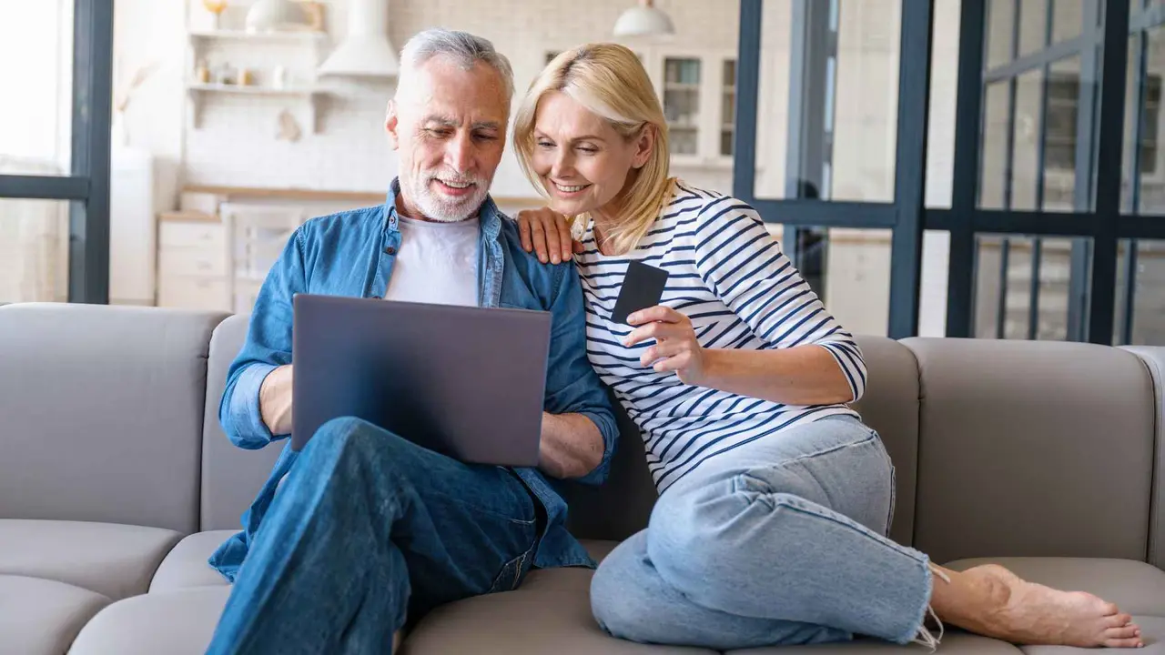 A couple uses their credit card as they shop online while holding their laptop.