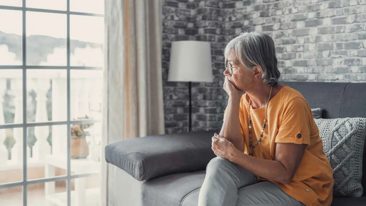 A sad woman is sitting on the sofa and looking out the window.