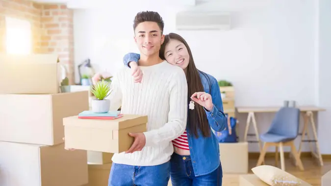 Young asian couple holding keys of new house, smiling happy and excited moving to a new apartment.