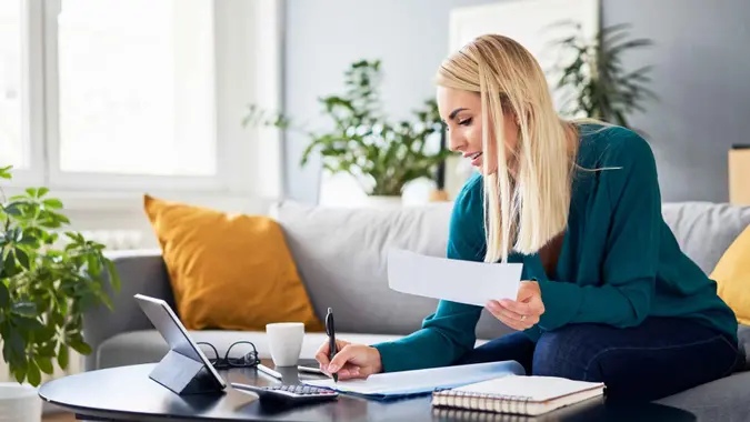 A woman sits on a couch and analyzes her bills.