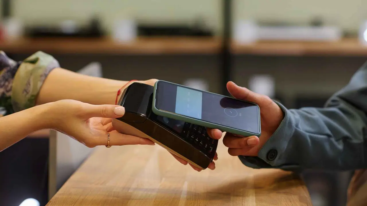 Side view closeup of young man paying with smartphone in tech store, copy space.