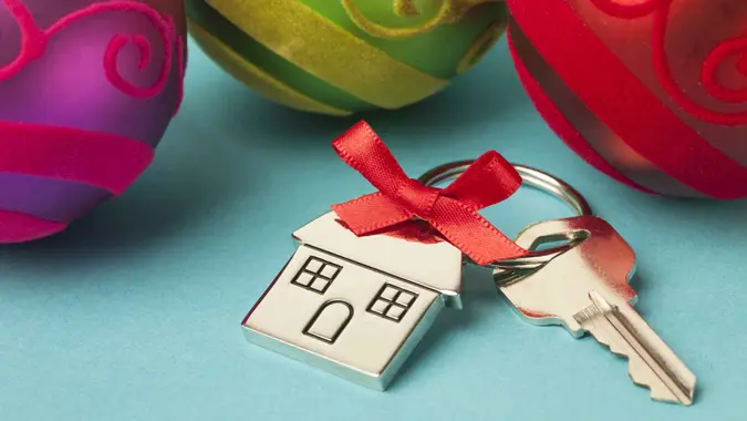House keys on house shaped keychain with a red ribbon and christmas ornaments on blue background.