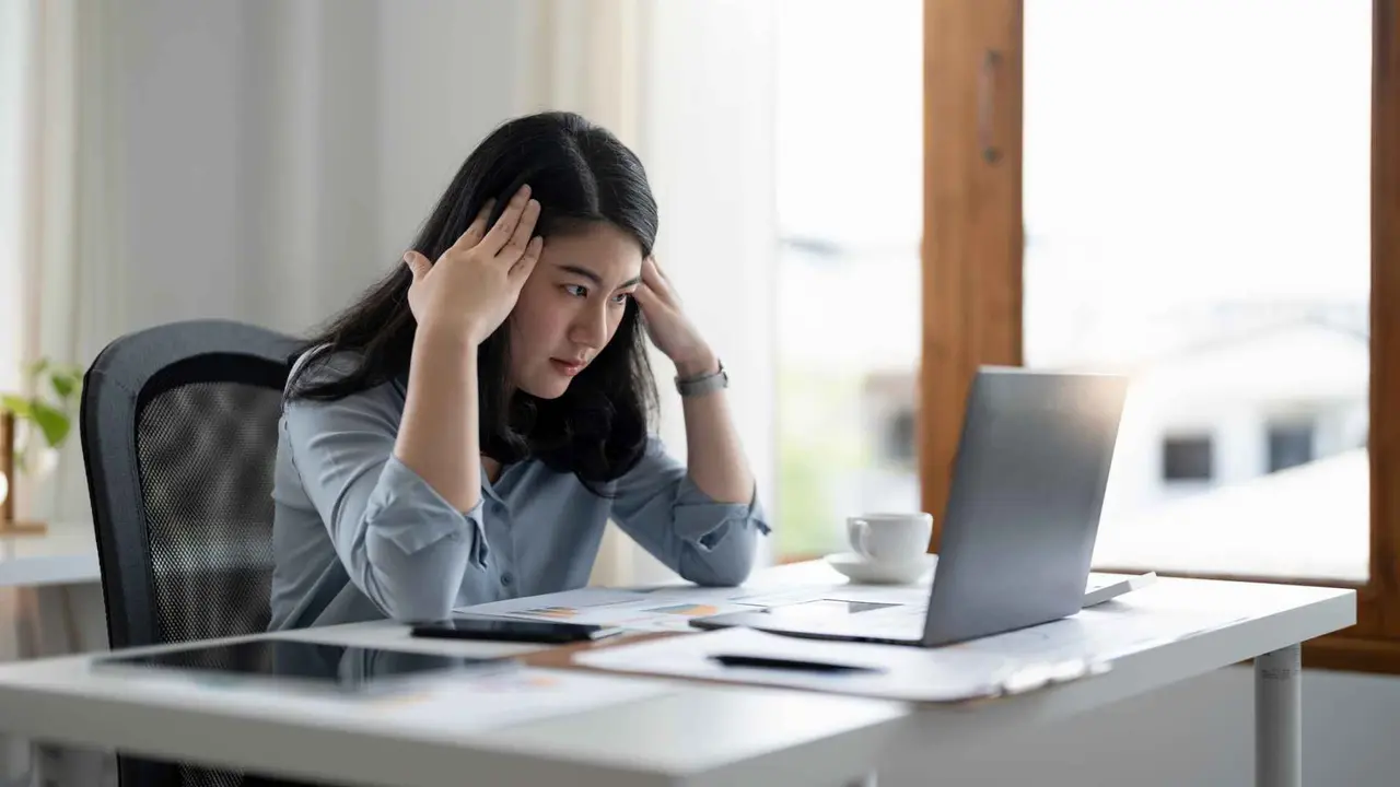 Stressed businessman is sitting at his desk with his hands on his head.