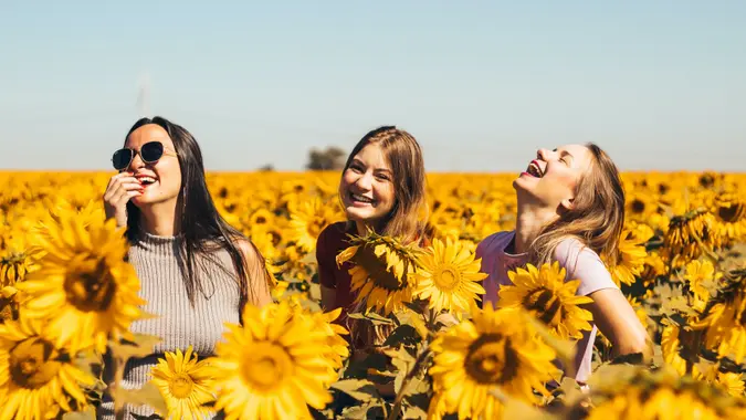 Group of friends smiling and standing among a field of sunflowers.