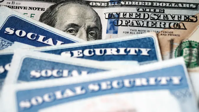 Several Social Security Cards on a US United States one hundred dollar bill $100 system of benefits for retired elderly people.