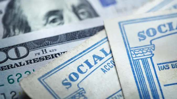 Two Social Security cards rest on top of several $100 bills.