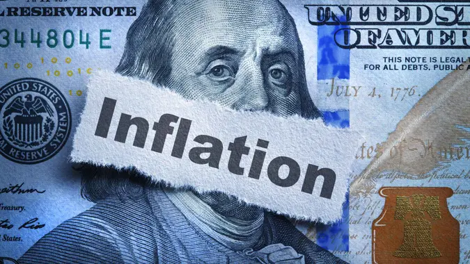 Inflation printed on a piece of torn paper that rests on top of the portrait of Benjamin Franklin on the one hundred dollar bill.