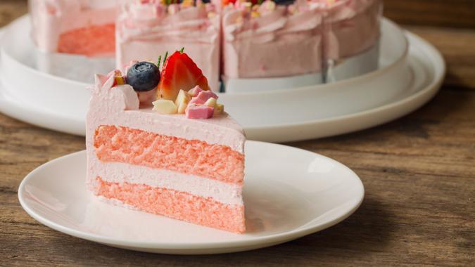 White chocolate strawberry yogurt cake decorated with fresh fruits and chocolate chunk on wood table.