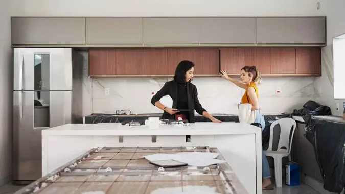 Two women architects inspecting kitchen and discussing the renovation plan at under construction site.