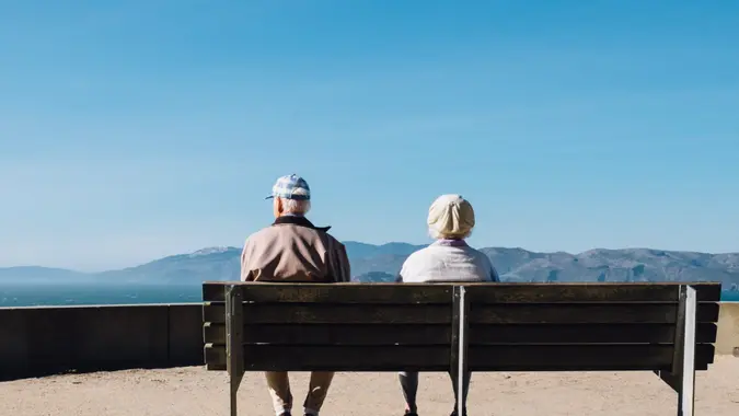 A retired couple sits on a bench and watches nature.